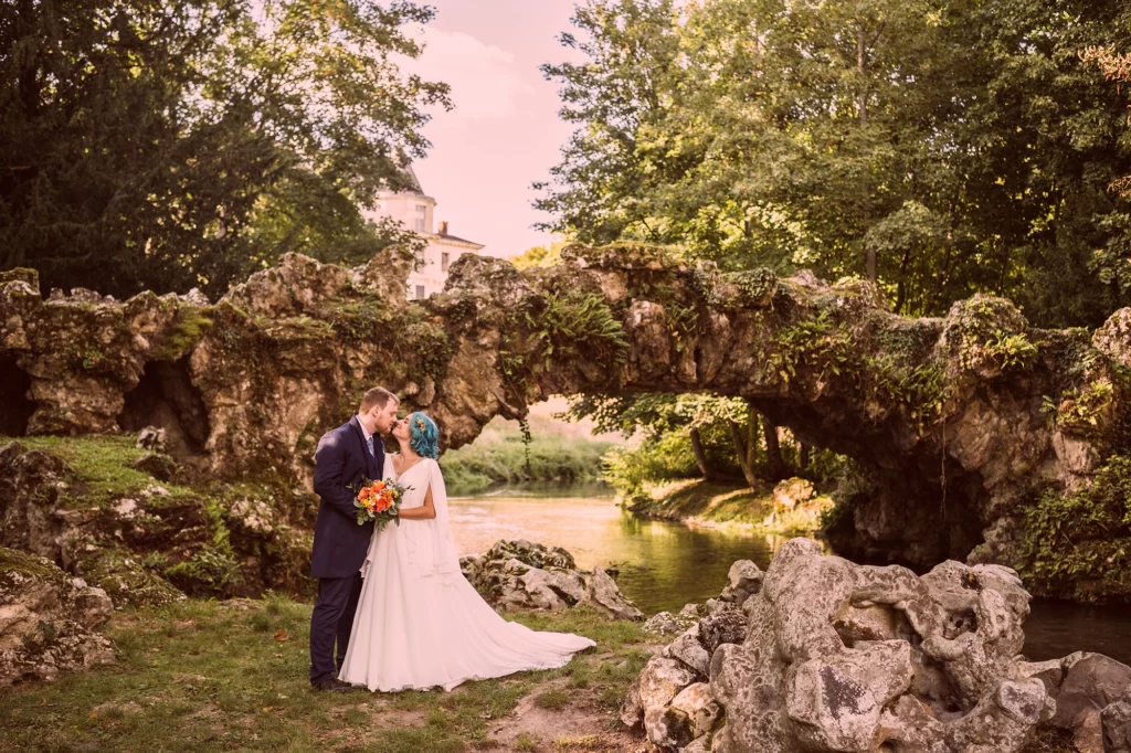 Couple de mariés dans la nature en séance photo de couple au Domaine de Méréville devant un vieux pont de pierre